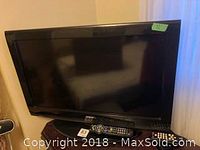 Front view of Toshiba 32-inch flatscreen TV showing screen and two remotes on stand.