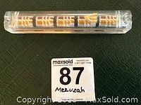 Top and angled side photo showing mezuzah in clear hard plastic case with tapestry inside and parchment klaf.