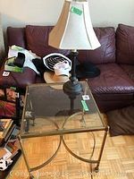 Full view of metal frame glass top table with table lamp on top in front of a couch