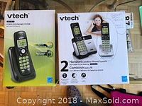 Photo showing two VTech cordless phone system boxes, one green single handset system and one larger two-handset system with a woman pictured on box.