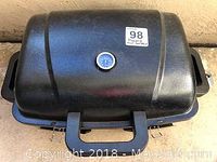 Closed view of black portable propane barbecue grill showing lid with temperature gauge and side handles.