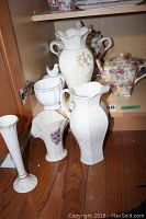 Seven ceramic items including Lenox vases and pitchers with floral designs, Neiman Marcus creamer and sugar, decorative covered bowl with grape and flower motif, and Wellbeck Royal Winton floral teapot.