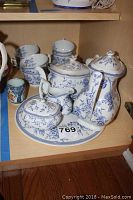 Full tea set with teapot, creamer, sugar bowl on a round tray, and four cups behind