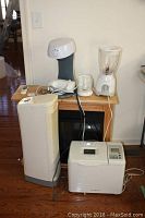Photo showing space heater, bread maker, blender, air filter, and coffee maker on wooden table with cords and remote controls