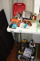 Wide view of a table showing various hand tools, orange power drill, screwdriver bit sets, and a yellow-black vacuum cleaner below.