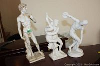 Three male nude resin statues displayed on a surface showing relative sizes and styles.