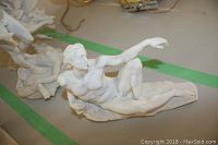 Reclining male nude statue in white resin, lying on a textured base part of the set.
