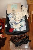 Tote filled with assorted quilts, linens, ball caps, and hangers, showing overall used condition.