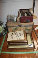 Woven rattan chest with palm tree designs on front, stacked with picture frames and Bath and Body Works gift set on top, Hideaways slipper box nearby.