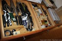 Drawers open showing assorted kitchen knives and tools including can opener, peelers, and kitchen shears with black and white handles.