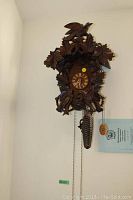 Full view of the hand-carved wooden cuckoo clock with pinecone weight and hanging chains.