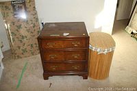 Chest of drawers marked Henredon with three brass-handled drawers and minor wear, next to the wooden hamper.