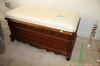 Full view of solid wood storage bench chest with upholstered beige cushion top, carved wood detail on front, and carved feet.