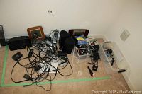 Wide view of assorted electronics on floor including clocks, chargers, phones, and speakers with tangled cords.