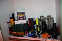 Shelf with multiple flashlights, two metal lanterns, and battery packs