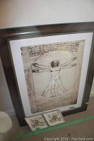 Framed Vitruvian Man print with two diamond-shaped ceramic floral pieces on floor beside it