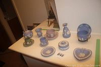 Side view of table displaying multiple Wedgwood Jasperware pieces including cups, saucers, vase, sugar bowl, trinket box, and decorative plates.