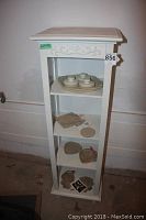 Full view of beige decorative accent shelf with assorted contents placed on each shelf level.