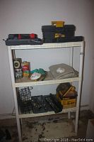 Full view of plastic shelving unit with tools on three shelves, including toolboxes, hardware, and rags.