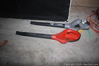 Two cordless leaf blowers, one Earthwise in grey and black and one Black & Decker in red and black, placed on a concrete floor.