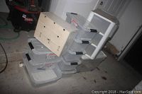 Seven stacked Iris plastic buckle-up storage boxes, a wooden multi-drawer organizer box on top, and a white Sterilite 3-drawer cart in the background.