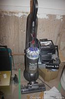 Full view of the Dyson DC65 vacuum cleaner upright with several boxed accessories nearby in a basement setting.