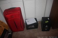 Red fabric suitcase alongside two black Sentry safes on carpeted floor in front of white folding closet doors.