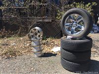 Four mounted tire-and-rim assemblies next to four unmounted silver rims
