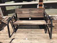 Front view of wood and metal swivel rocker bench on wooden deck.