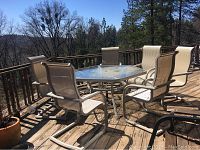 Wide angle showing the outdoor patio table and six matching chairs positioned on a wooden deck with natural surroundings.