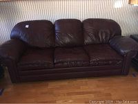 Full view of the brown leather sofa bed, showing three cushions and wide armrests on a wood floor.