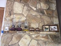 Photo of three glass oil lamps, three metal decorative spheres, two framed bird prints, and wood carved duck on stone mantle