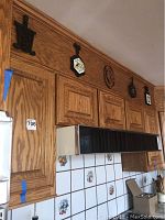 Wide view of kitchen upper wooden cabinets with several trivets and art plates displayed above cabinet tops.