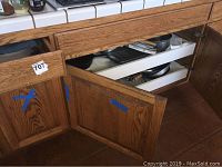 Kitchen cabinet with open doors, showing white pull-out drawers containing cooking pots and pans.