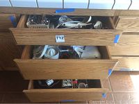Open wooden drawers showing mixed kitchen utensils and tools including ladles, spatulas, peelers, slicers, and juicers