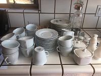 Top down view of white china set showing stacked plates, cups, creamers, sugar bowls, and some tumblers.