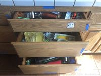 Open drawer showing various thermal cups, metal cups, and assorted kitchenware including glass, plastic containers, and kitchen tools.