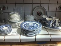 Full set arranged on countertop showing stacks of plates, bowls, and cups with saucers in classic blue and white patterns consistent with Churchill England Willow and J&G Meakin Classic Blue Nordic.