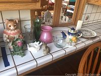 Full view of 17 assorted decorative items including ceramic cat figurine, glass vases, teapot, bowl, and a limited edition plate.