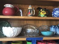 Shelf display of mixed bowls, beer stein, and vases showing variety of items including several ceramic pitchers and glass bowls.