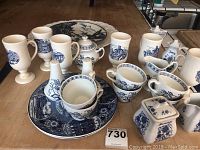 Photo showing 22 blue and white tea ware pieces including footed mugs, cups, plates, small teapot, creamers, and salt and pepper shakers arranged on kitchen counter.