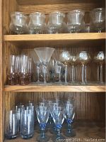 Multiple shelves of assorted glassware including small stemmed glasses, a martini-style glass, and drinking glasses.
