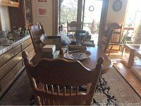 Dining table and six wooden chairs in a sunlit room, showing full table and chairs from side and end views.