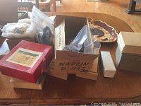 Overall view of cardboard boxes containing various napkin rings and other items on a wooden table