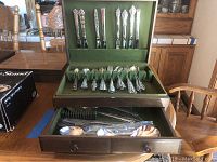 Wooden chest showing mixed utensils in green velvet liner with two storage drawers open.