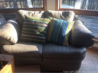 Full front view of grey leather loveseat with two striped throw pillows.