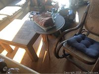 Photo showing wooden side table with parquet pattern top and nearby rocking chair with cushions and folded textiles