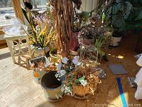 Wide shot showing multiple ceramic plant pots, some with faux plants, and white metal plant stands in natural sunlight on wooden floor