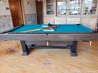 Front view of full pool table with cues, rack and box on playing surface