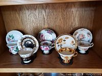 Photo showing six teacup and saucer sets on a shelf with varied floral and ornate designs